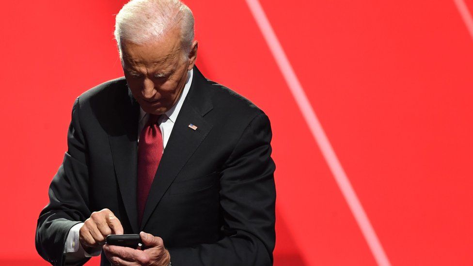 Joe Biden taps on a phone against a red backdrop in this 2019 file photo