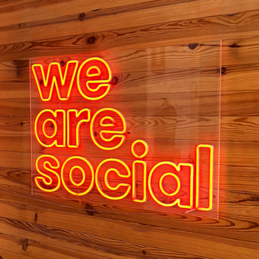 We Are Social Logotype in Red Neon over a Wood paneled wall